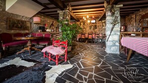 A rustic interior with stone walls, wooden beams, a stone floor, a red chair, a table with a checkered tablecloth, and a chandelier. - 15th century castle, between Cinque Terre and Portofino, private pool, sea view (Leivi)