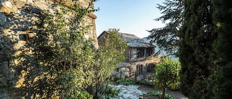 Ein Steingebäude mit rustikalem Äußeren, umgeben von üppiger Vegetation und einem Steinweg, der zu einer Holzhütte führt.