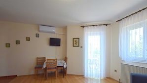 A room with a wooden floor, a dining table with chairs, a TV mounted on the wall, and a window with curtains. - Apartment Frane 2 with Seaview (Vantačići)