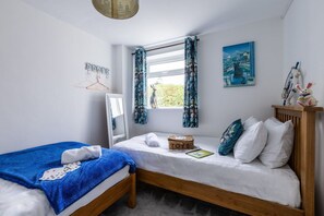 A bedroom with two single beds, a window with curtains, a wall-mounted shelf with toys, and a painting.