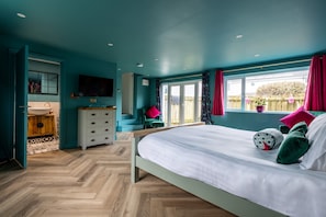 Een slaapkamer met een bed, een dressoir, een televisie en een raam met gordijnen.