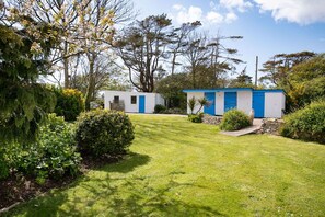 A small, white building with a blue door, surrounded by a well-maintained lawn and various shrubs.