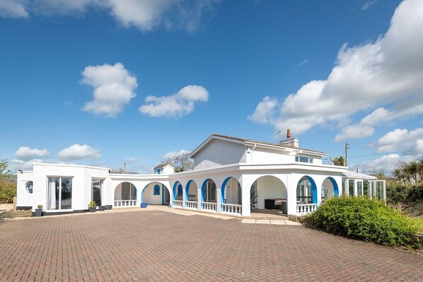 A white building with blue arches and a brick driveway.