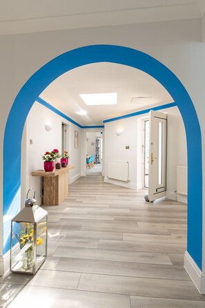 A hallway with a blue archway, wooden flooring, a small table with potted plants, and a decorative lantern.