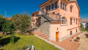 A two-story house with a stone staircase leading to the entrance, surrounded by a well-maintained garden.
