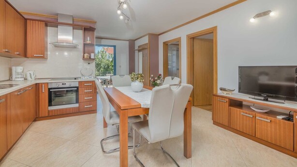 A modern kitchen with wooden cabinets, a dining table with chairs, a TV, and a ceiling light fixture.