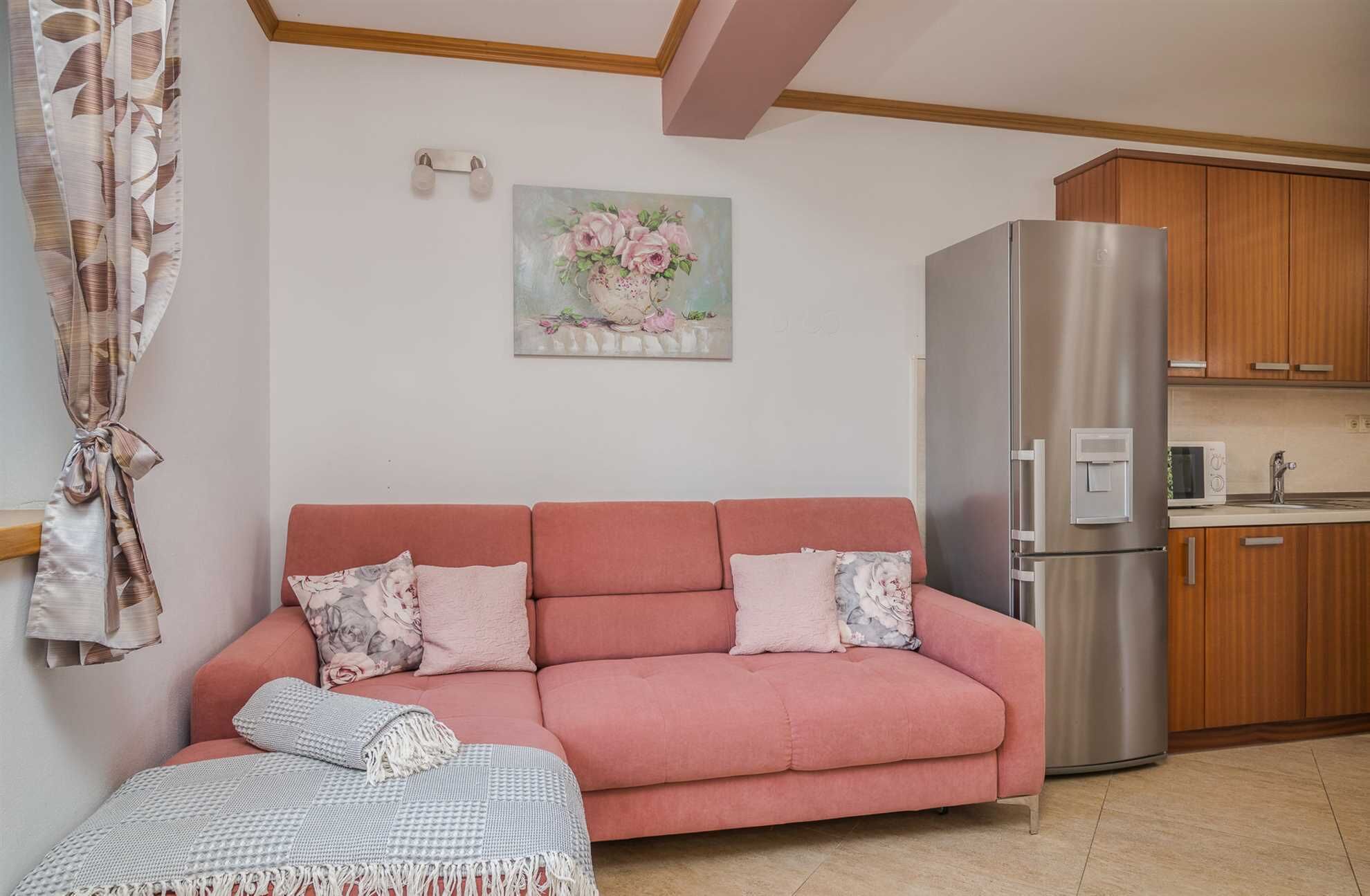 A living room with a pink sofa, a blanket, and a painting of flowers on the wall.