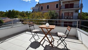 En tagterrasse med et træbord og to stole, en hvid, rund genstand på bordet, og en bygning med balkoner i baggrunden.