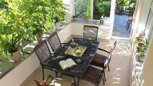 Een overdekt terras met een tafel en stoelen, omgeven door potplanten en uitzicht op de tuin.