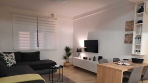Een moderne woonkamer met een bank, een salontafel, een televisie en een eethoek met stoelen en een tafel.