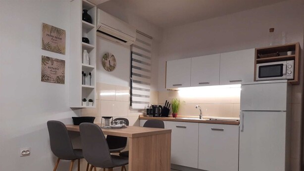 Een moderne keuken met witte kasten, een magnetron en een gootsteen. Er zijn twee stoelen en een klein tafeltje.