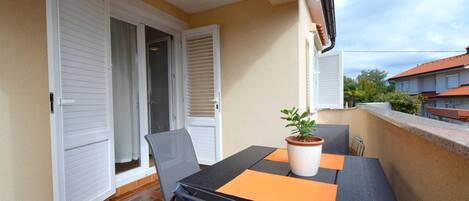A balcony with a table, chairs, and a potted plant.