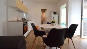 Une cuisine moderne avec des meubles blancs, un four encastré et un coin repas comprenant une table ronde et des chaises noires.