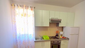 A small kitchen with light green cabinets, a gas stove, a sink, and a refrigerator.
