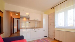 Cocina compacta con gabinetes blancos, extractor de acero inoxidable y ventana con cortinas translúcidas.