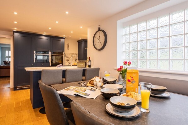 A modern kitchen with dark cabinets, a dining area with a table set for breakfast, and a large window with frosted glass.
