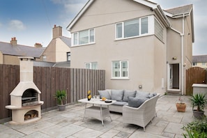 A residential backyard with a built-in outdoor oven, a seating area with a sofa and table, and potted plants.