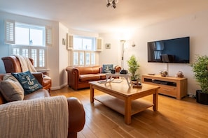 A living room with a brown leather sofa, a wooden coffee table, a flat-screen TV, and a potted plant. - Ancones: A fabulous house with beach views (Rhosneigr)