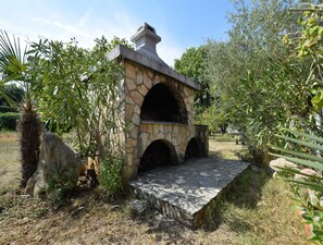 Una edificación de piedra con chimenea, aberturas en arco y un camino de piedra que conduce a ella.