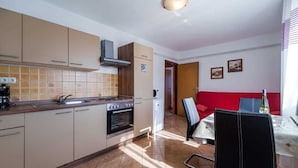 A compact kitchen with a stove, oven, and a dining area with a red sofa and a table. - Apartment Anka 2 with Balcony (Krk)