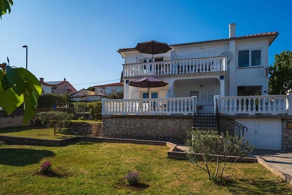 Ein zweistöckiges Gebäude mit Balkon, Garage und gepflegtem Rasen.