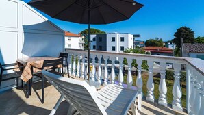 A balcony with a table and chairs, a large umbrella, and a white balustrade. - Apartment Anka 2 with Balcony (Krk)