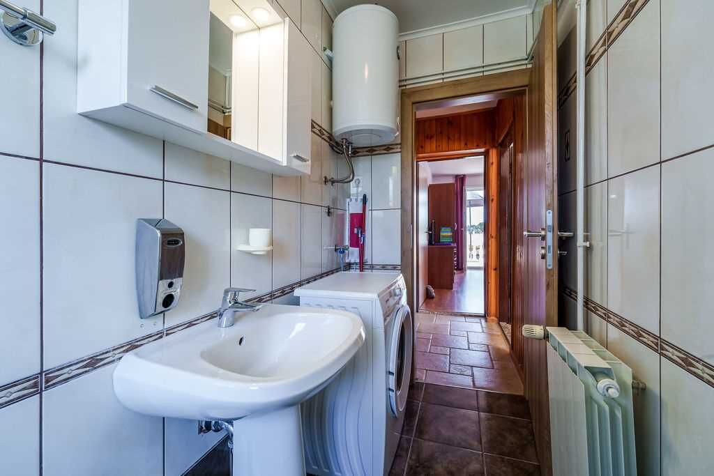 A bathroom with a sink, a washing machine, and a mirror.