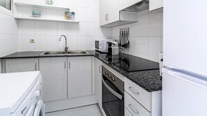 Cocina compacta con armarios blancos, encimera de granito, horno integrado, microondas y lavavajillas.