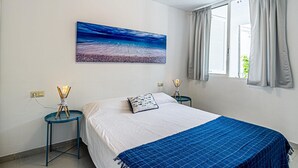 Un dormitorio con una cama grande, una mesita de noche, una lámpara de pared y un ventanal con cortinas.