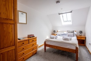 A bedroom with a wooden bed, a dresser, a bedside table with lamps, and a window. - Y Stabl: Pet-friendly cottage with stunning views (Ty Cros)