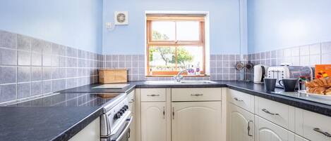Cocina compacta con armarios blancos, encimera negra y ventana con vistas.