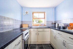 A compact kitchen with white cabinets, a black countertop, and a window with a view. - Y Stabl: Pet-friendly cottage with stunning views (Ty Cros)