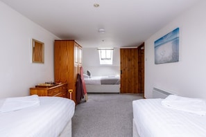 A room with two beds, a wooden wardrobe, a small desk with chess pieces, a radiator, and a painting on the wall. - Y Stabl: Pet-friendly cottage with stunning views (Ty Cros)