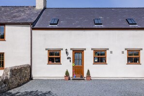 A two-story building with a white facade, a wooden door, and multiple windows. - Y Stabl: Pet-friendly cottage with stunning views (Ty Cros)