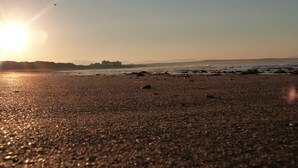 Une plage au coucher du soleil, avec un bâtiment visible au loin et un ciel dégagé.