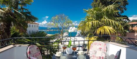 A balcony with a table set for two, overlooking a marina with boats and a clear blue sky.