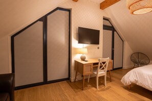A bedroom with a sloped ceiling, a desk with a lamp, a bed, and a television mounted on the wall. - Porth Crigyll: Beachfront holiday cottage on Anglesey (Rhosneigr)