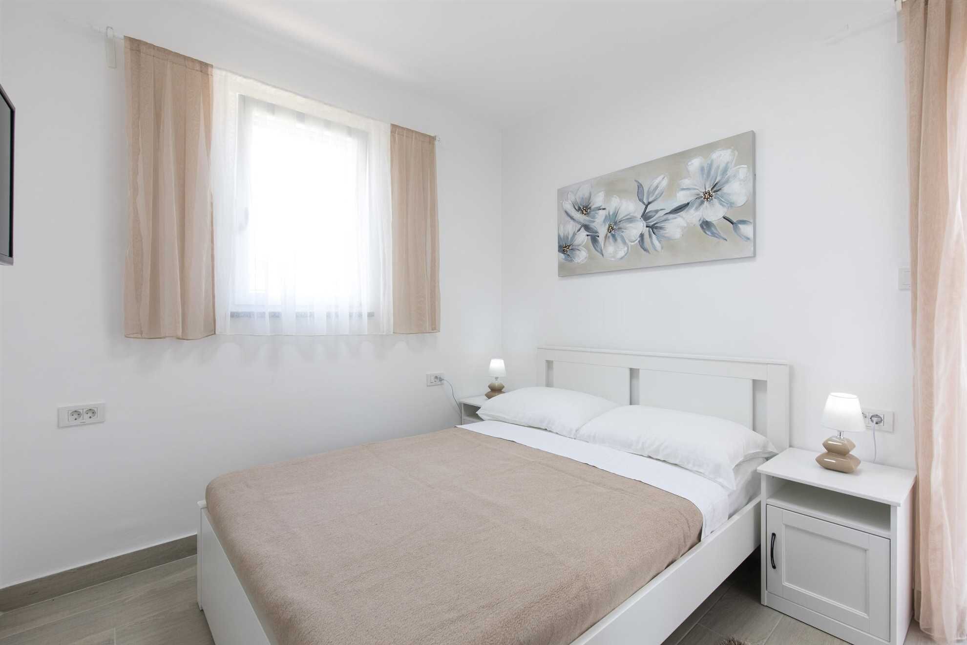 A bedroom with a bed, nightstands, a painting, and a window with curtains.