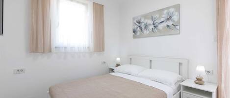 A bedroom with a bed, nightstands, a painting, and a window with curtains.