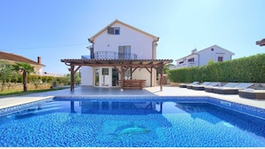 Una casa con piscina, una pérgola de madera y una banca.