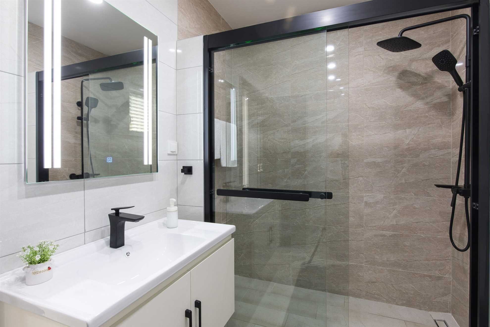 Un bagno moderno con doccia vetrata, lavandino bianco con rubinetto nero e specchio sopra il lavandino.