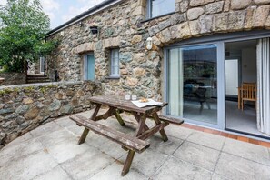 A stone building with a wooden picnic table and a glass door leading to an interior space.