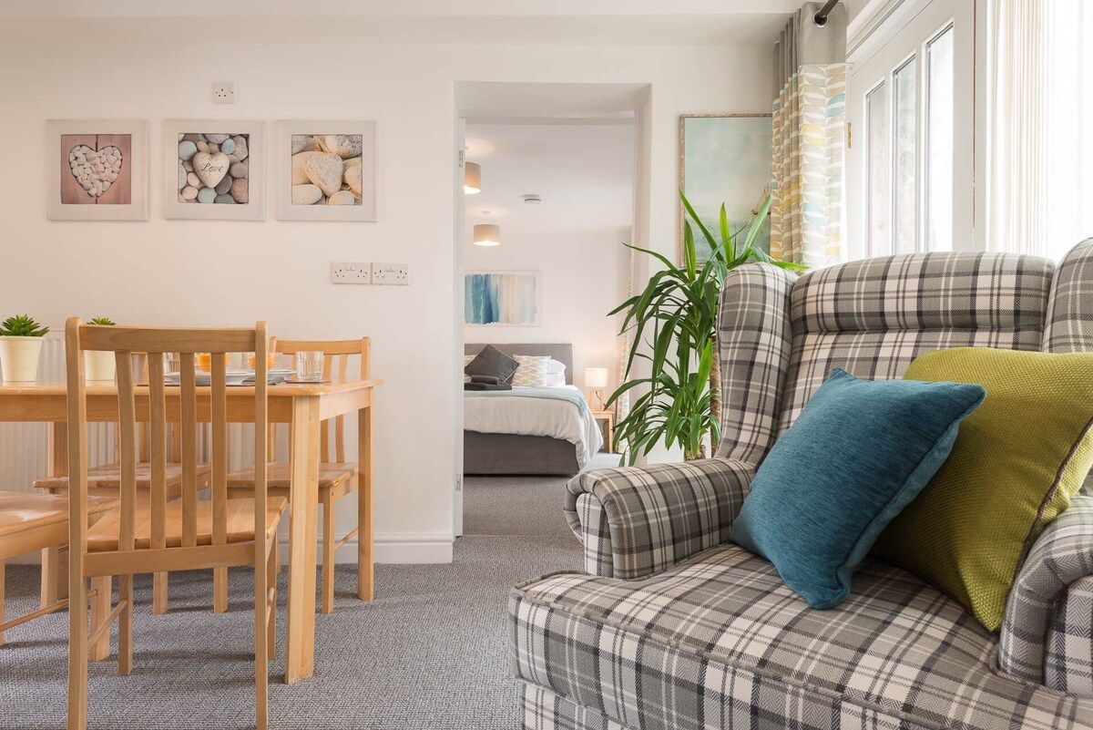 Un salon chaleureux avec un canapé à carreaux, une table à manger avec des chaises et un lit en arrière-plan.