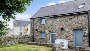 A stone building with a grey door, a window, and a small air conditioning unit outside. - Ty Arthur: Ground-Floor Apartment for Two in Aberffraw | Managed by Anglesey Holiday Lettings (Ty Croes)