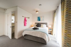 A hotel room with a bed, a bedside table with a lamp, a door leading to a bathroom, and a window with curtains.