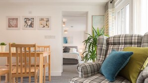 A cozy living room with a plaid sofa, a wooden dining table, and a green plant. - Ty Arthur: Ground-Floor Apartment for Two in Aberffraw | Managed by Anglesey Holiday Lettings (Ty Croes)