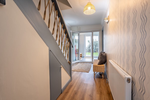 A hallway with a wooden floor, a staircase with rope decor, a wicker basket, and a radiator.