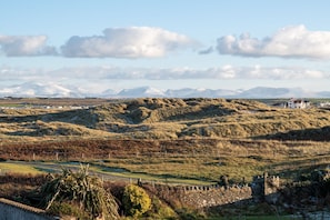 A rural landscape with rolling hills, a stone wall, and a distant white building.
