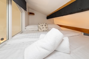 A bedroom with a bed, pillows, a window, and a wooden headboard. - Lakeside : Stylish 4‑Bed Family Villa in Rhosneigr | Managed by Anglesey Holiday Lettings (Rhosneigr)