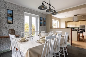 A dining area with a table set for four, white chairs, and a patterned wallpaper. - Lakeside : Stylish 4‑Bed Family Villa in Rhosneigr | Managed by Anglesey Holiday Lettings (Rhosneigr)